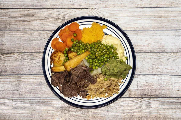 Sunday dinner of slow cooked shredded pulled beef on a plate with plenty of vegetables such as peas, mushy peas, parsnips, roast potatoes and carrots, stock photo image