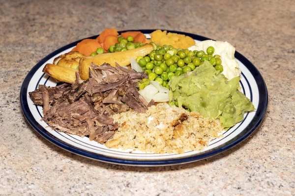 Sunday dinner of slow cooked shredded pulled beef on a plate with plenty of vegetables such as peas, mushy peas, parsnips, roast potatoes and carrots, stock photo image