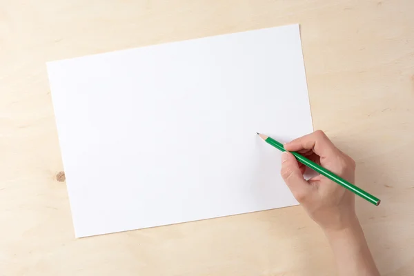 One arm holds pencil on white paper on wooden table
