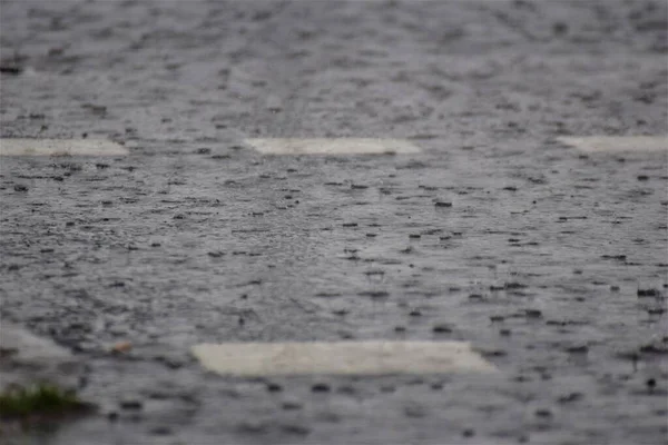 Pioggia su strada asfaltata grigio scuro con segnaletica stradale bianca — Foto Stock