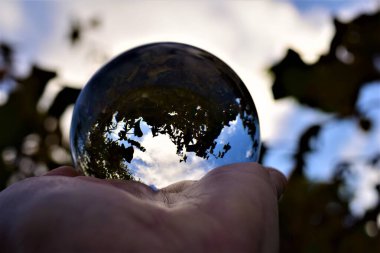 Gökyüzü ve ağaçlar, mavi gökyüzüne ve dallara karşı bir eldeki mercek topunun içinden geçer.