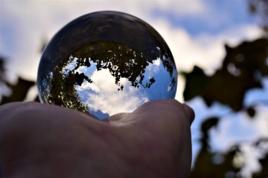 Gökyüzü ve ağaçlar, mavi gökyüzüne ve dallara karşı bir eldeki mercek topunun içinden geçer.