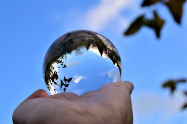 Gökyüzü ve ağaçlar, mavi gökyüzüne ve dallara karşı bir eldeki mercek topunun içinden geçer.