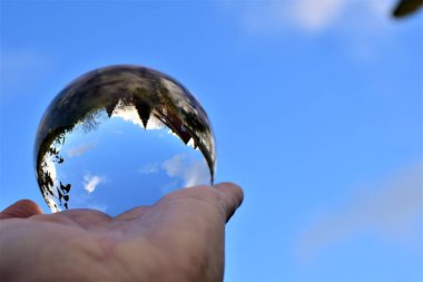 Mavi gökyüzü ve bazı ağaçlar bir insan elinin üzerinde kristal bir mercek topunun içinden geçer.