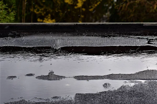 Pioggia leggera su un tetto piatto nero su uno sfondo verde — Foto Stock