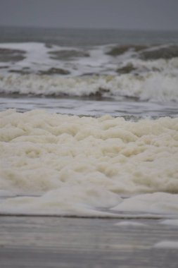 Bulutlu bir günde Kuzey Denizi sahilinde dalgalar ve deniz köpüğü