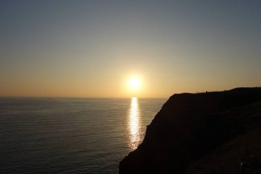 Önünde bir uçurum olan deniz kenarında gün batımı