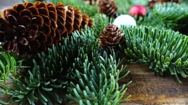 Eski ahşap bir tahtanın üzerinde koni ve Noel topları olan bebek nobilis dalları.