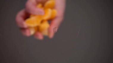 Soyulmuş mandalina dilimleri cam bir yüzeye düşer. Alt manzara. Yavaş çekim.