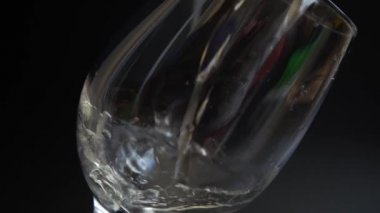 Şarap siyah arka planda bir bardağa dökülür. Yavaş çekim.