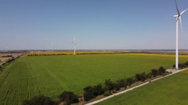 Rüzgar türbini ve tarımsal alanların üzerinde uçan bir dron görüntüsü. Ayçiçeği tarlası. Yel değirmeni. Rüzgar çiftliği.