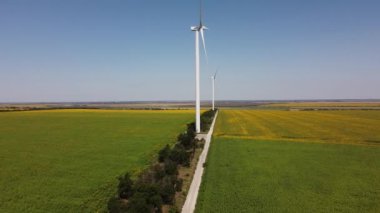 Rüzgar türbini ve tarımsal alanların üzerinde uçan bir dron görüntüsü. Ayçiçeği tarlası. Yel değirmeni. Rüzgar çiftliği.