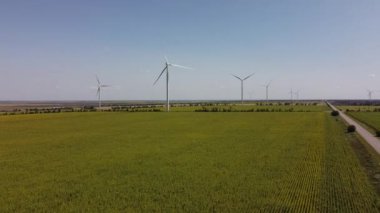 Rüzgar türbini ve tarımsal alanların üzerinde uçan bir dron görüntüsü. Ayçiçeği tarlası. Yel değirmeni. Rüzgar çiftliği.