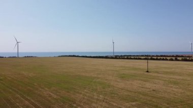Rüzgar türbini ve tarımsal alanların üzerinde uçan bir dron görüntüsü. Denizin arka planında yel değirmenleri. Yel değirmeni. Rüzgar çiftliği. 