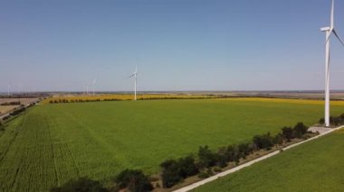 Rüzgar türbini ve tarımsal alanların üzerinde uçan bir dron görüntüsü. Ayçiçeği tarlası. Yel değirmeni. Rüzgar çiftliği. 