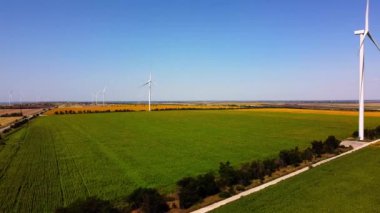 Rüzgar türbini ve tarımsal alanların üzerinde uçan bir dron görüntüsü. Ayçiçeği tarlası. Yel değirmeni. Rüzgar çiftliği.