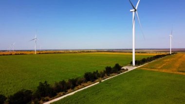 Rüzgar türbini ve tarımsal alanların üzerinde uçan bir dron görüntüsü. Ayçiçeği tarlası. Yel değirmeni. Rüzgar çiftliği.