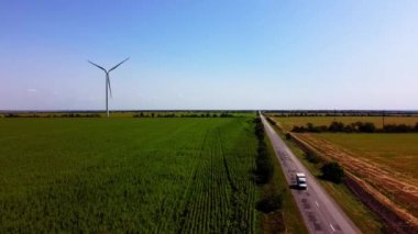 Rüzgar türbini ve tarımsal alanların üzerinde uçan bir dron görüntüsü. Ayçiçeği tarlası. Yel değirmeni. Rüzgar çiftliği.