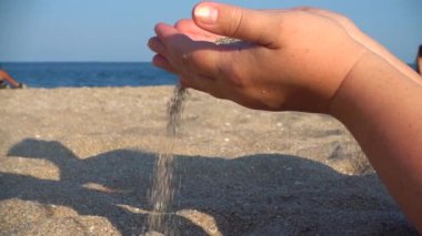 Kum, kadının elinden denizin arka planına düşer..