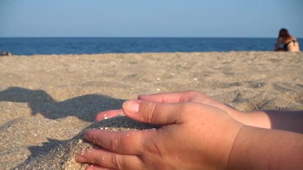 모래는 여자의 손에서 바다를 배경으로 떨어지고 — 비디오
