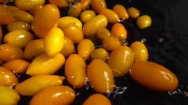 Sarı kiraz domatesi suya dökülüyor. Domates yıkıyorum. Siyah bir arka planda. Yavaş çekim.