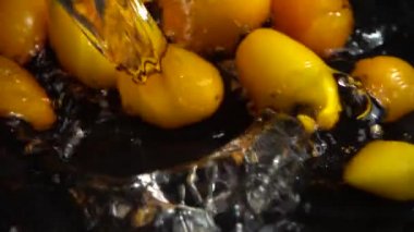 Sarı kiraz domatesi suya dökülüyor. Domates yıkıyorum. Siyah bir arka planda. Yavaş çekim.