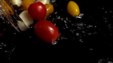 Suya kırmızı ve sarı kiraz domatesleri ve sarımsak dökülüyor. Domates yıkıyorum. Siyah bir arka planda. Yavaş çekim.