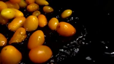 Sarı kiraz domatesi suya dökülüyor. Domates yıkıyorum. Siyah bir arka planda. Yavaş çekim.