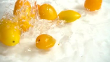 Sarı kiraz domatesi suya dökülüyor. Domates yıkıyorum. Beyaz bir arka planda. Yavaş çekim.