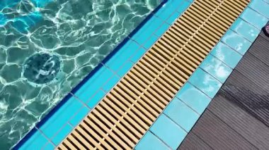 Açık havuz alanı. Güneş ışığı berrak suda parlıyor ve havuz kenarında mavi fayanslar var..