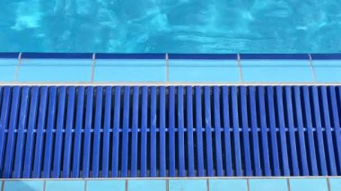 Açık havuz alanı. Güneş ışığı berrak suda parlıyor ve havuz kenarında mavi fayanslar var..