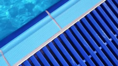 Açık havuz alanı. Güneş ışığı berrak suda parlıyor ve havuz kenarında mavi fayanslar var..