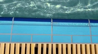 Açık havuz alanı. Güneş ışığı berrak suda parlıyor ve havuz kenarında mavi fayanslar var..