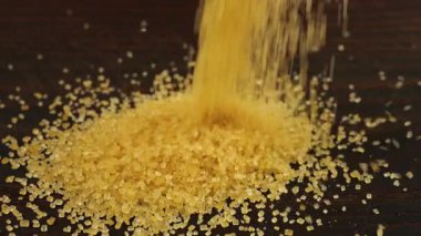 Kahverengi şeker kristalleri koyu kahverengi ahşap bir yüzeye serpiştirilir. Bir yığın şeker, bir sürü şeker..