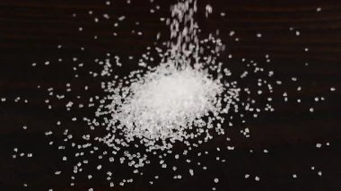 Beyaz şeker kristalleri koyu kahverengi ahşap bir yüzeye serpilmiştir. Büyük bir şeker yığını, bir sürü şeker. Yavaş çekim.