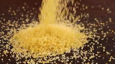 Kahverengi şeker kristalleri koyu kahverengi ahşap bir yüzeye serpiştirilir. Büyük bir şeker yığını, bir sürü şeker. Yavaş çekim.