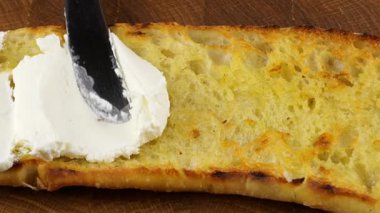 Zeytin yağında kızartılmış ve boydan boya kesilmiş ev yapımı ciabatta ekmeğinin yarısı süzme peynirle bıçakla yayılıyor..