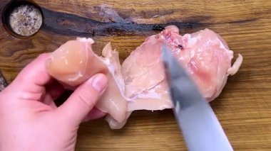 Evdeki tahta bir tahtanın üzerinde çiğ tavuk göğsünü bıçakla kesip budamak. Tahta meşe kesme tahtası..