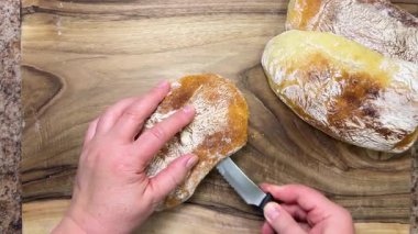 Yeni pişmiş, lezzetli bir ciabatta somunu tahta bir tahtanın üzerinde uzunlamasına ikiye bölünür. Ciabatta ceviz ağacından kesme tahtasında.