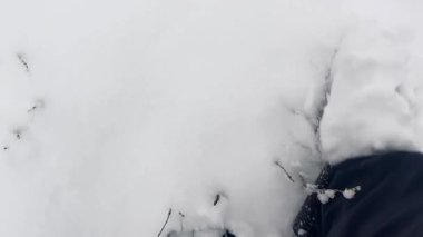 Koyu kırmızı bağcıklı koyu renk kış botları giyen biri, derin ve el değmemiş karların içinden birinci şahıs perspektifinden görülür..