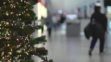 Bir Noel ağacı bir alışveriş merkezinde ışık ve süslemelerle süslenir. Bulanık bir insan figürü kalabalık, parlak koridor alışveriş merkezinde yürüyor..