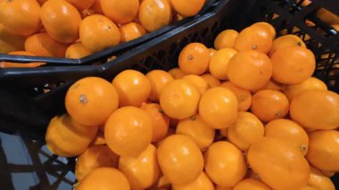 Süpermarkette siyah plastik sandıklara doldurulmuş taze portakallar. Çok sayıda olgun, sarı-turuncu turunçgil meyvesinin satışa hazır görüntüsü..