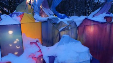 LVIV, UKRAINE - 06 Ocak 2026: Karla kaplı tek boynuzlu at heykeli gece parlak mavi ve pembe ışıkla parlıyor. Parkta çekim..