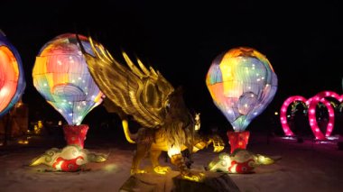 LVIV, UKRAINE - Ocak 06, 2026: Kış harikalar diyarı parlak fenerlerle aydınlatıldı. Gece gökyüzünün altında parlayan altın Griffin heykeli. Sihirli, parlayan sıcak hava balonları ve efsanevi yaratıklar..