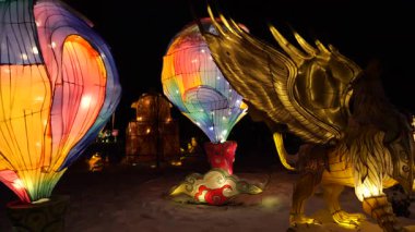 LVIV, UKRAINE - Ocak 06, 2026: Kış harikalar diyarı parlak fenerlerle aydınlatıldı. Gece gökyüzünün altında parlayan altın Griffin heykeli. Sihirli, parlayan sıcak hava balonları ve efsanevi yaratıklar..