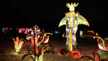 LVIV, UKRAINE - Ocak 06, 2026: Karlı bir parkta aydınlatılmış savaşçı kraliçe heykeli. Renkli fener figürleri büyülü bir kış harikalar diyarı gösterisi yaratıyor..