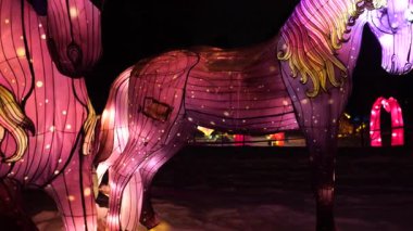 LVIV, UKRAINE - OCAK 06, 2026: Karlı bir kış parkında at şeklinde parlak fenerler, parıldayan hayvan figürleriyle büyülü bir gece sahnesi, neşeli ışık gösterisi tuhaf bir atmosfer yaratıyor.