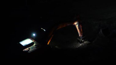 Bir kazıcı gece bir inşaat alanında çalışıyor. Endüstriyel makine dünyayı kazıyor, parlak lambalarla aydınlatılıyor..