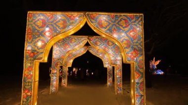 Kış parkı ortamında aydınlatılmış dekoratif kemerler. Aydınlatılmış yapılarda canlı mavi ve kırmızı desenler.