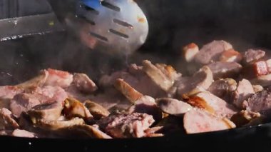 Sosis ve et sıcak bir tavada cızırdıyor. Buhar yükselirken yemek pişirme işlemini yakından çek. Sokak yemekleri hazırlanıyor..